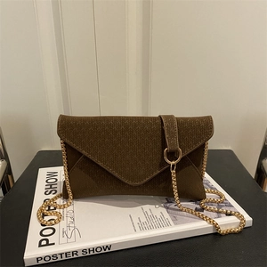 Brown woven envelope crossbody bag with gold chain strap on a white book base
