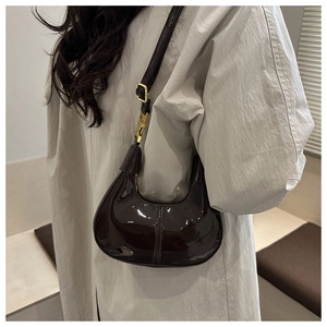 Close-up of a dark burgundy patent leather crescent bag worn with an ivory coat