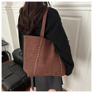 Close-up of brown suede tote bag featuring vertical silver rivets on a shoulder strap