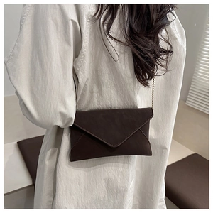 Detail of dark brown envelope crossbody bag with gold chain strap and suede texture