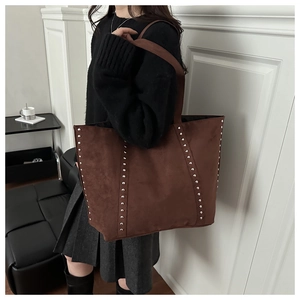 Close-up of deep brown suede tote bag featuring decorative silver metal rivets and straps