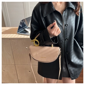 Detail of beige saddle bag with unique gold twisted handle on black leather coat
