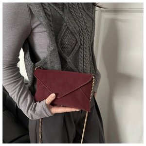 Detail of burgundy envelope chain bag in frosted texture on female model's side