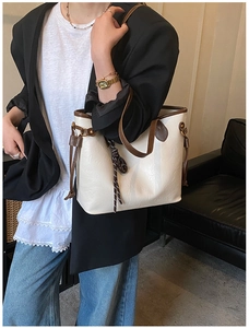 Detail view of cream leather tote bag with brown contrast trim and woven rope charm