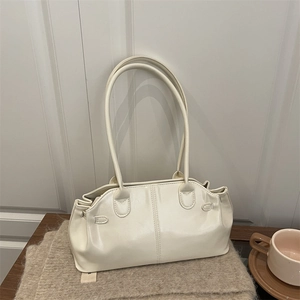 Minimalist creamy white glossy leather tote bag with long straps on a cozy knit blanket