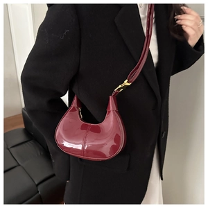 Detail view of burgundy crescent bag with glossy finish and chic gold metal buckles