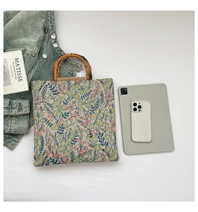Flat lay of floral canvas tote bag with bamboo handles next to a tablet and denim jacket