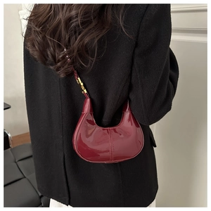 Detail of burgundy patent leather crescent bag with glossy finish and gold metal hardware