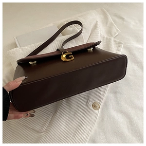 Detailed view of dark brown crossbody bag with gold G-shaped metal buckle and suede flap