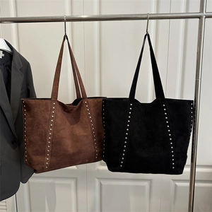 Brown and black oversized faux suede tote bags with silver rivets on metal display stand