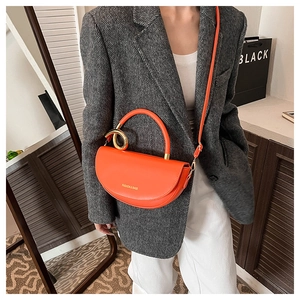 Detail of vibrant orange crescent saddle bag with metallic ring and adjustable strap