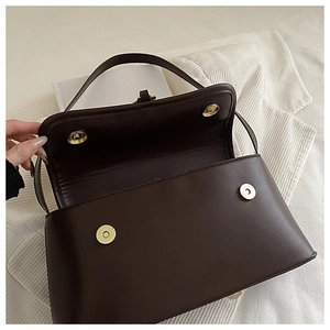 Detail of dark brown leather handbag showing double magnetic closure and gold hardware