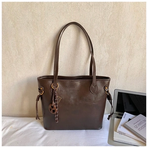 Detail of a large dark brown tote bag with decorative drawstrings and a cute charm