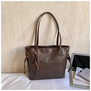 Detail of a brown tote bag with premium leather texture and a unique cookie-shaped charm