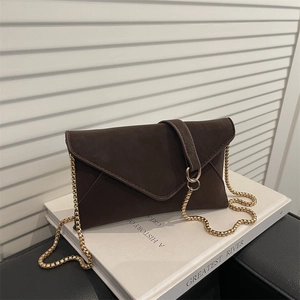 Dark brown suede envelope crossbody bag with a gold chain strap on a white book