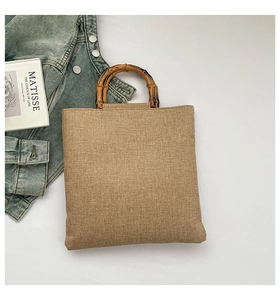 Detail of woven tote bag featuring natural bamboo handles and textured linen fabric