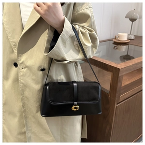 Close-up of black leather baguette bag featuring a vintage gold G-shaped metal buckle