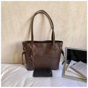 Detail of vintage dark brown leather tote bag with side drawstring and round charm accessory