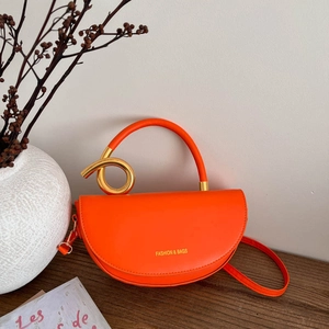 Sac selle orange vif avec nœud métallique doré et poignée sur fond de bois