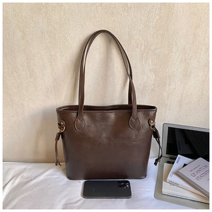 Detail of dark brown leather tote bag with side drawstring and golden metal eyelets