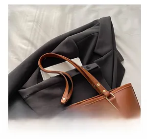 Detail of brown tote bag with reinforced handles, gold rivets, and embossed logo patch