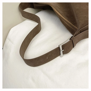 Detail of silver buckle and zipper on dark brown suede shoulder bag with matte finish