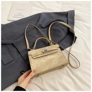 Sac à main mat kaki avec fermoir argenté posé sur un blazer gris et des draps blancs