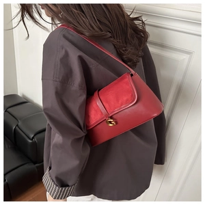 Close-up of red leather underarm bag featuring a gold G-shaped metal buckle on the strap