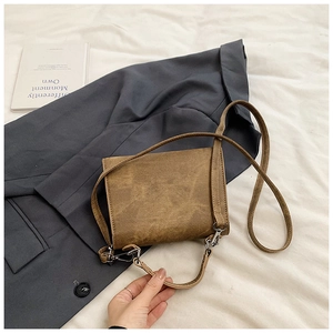 Vue détaillée d'un sac bandoulière vintage en cuir marron avec fermoir argenté sur un blazer