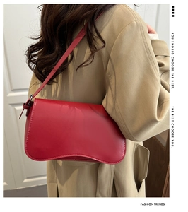 Dettaglio borsa a mezzaluna in pelle rossa con cuciture su sfondo trench beige