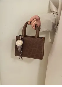 Detail of leopard embossed texture on a brown faux leather tote bag with fluffy pendant