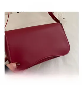 Dettaglio di una borsa sottobraccio in pelle bordeaux con patta curva dal taglio a onda