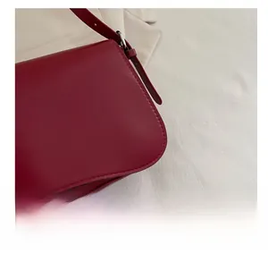 Dettaglio ravvicinato della borsa sottobraccio in pelle rosso scuro con cuciture e fibbia argento