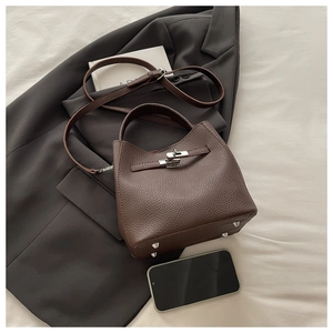 Detail of dark brown pebble leather bag with twist lock on grey blazer background