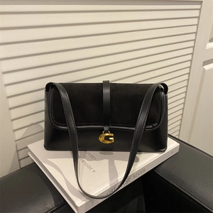 Minimalist black leather underarm bag with gold G buckle on white books backdrop