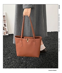 Detail of brown leather tote bag with grainy texture and golden V-shaped metal buckle