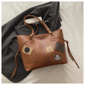 Detail of brown PU leather tote bag with vintage patches and side drawstring accents