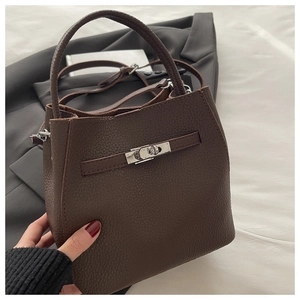 Detail of dark brown pebble leather handbag with silver twist lock and slim shoulder strap