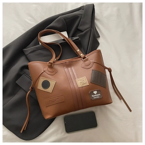 Detalle del bolso tote de cuero PU marrón con parches vintage y borlas sobre lino