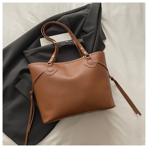 Detalle del bolso tote marrón con borlas sobre fondo de chaqueta negra y libro