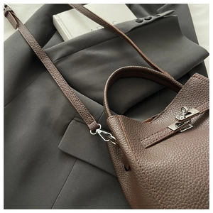 Detailed macro of dark brown lychee leather texture and silver buckle on a luxury handbag