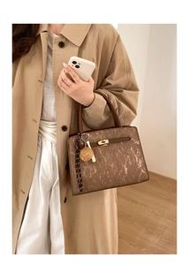Detail of a brown corduroy tote bag featuring a gold metal twist lock and striped ribbon charm
