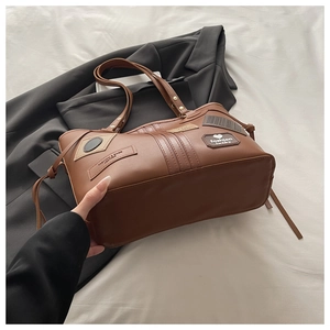 Close-up of brown PU leather tote bag featuring vintage patches and fashion brand labels
