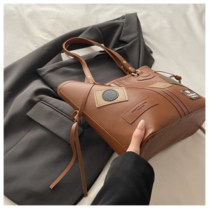 Close-up of brown PU tote bag with fashion lettering and heart patch on white sheets