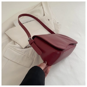 Dettaglio della borsa sottobraccio bordeaux in pelle lucida con fibbia argento su blazer bianco