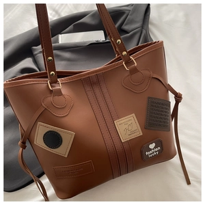 Detail of a brown PU leather tote bag with vintage patches and gold metal rivets