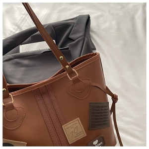 Macro view of brown PU leather tote bag with vintage patches and gold ring hardware