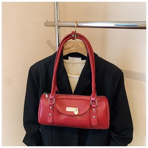 Détail d'un sac bowling rouge avec pendentif cœur et rivets argentés sur un costume noir