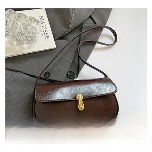 Detail of dark brown glossy leather underarm bag with gold-tone buckle on a blazer