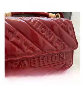 Detail of red patent leather handbag featuring quilted texture and embossed fashion letters
